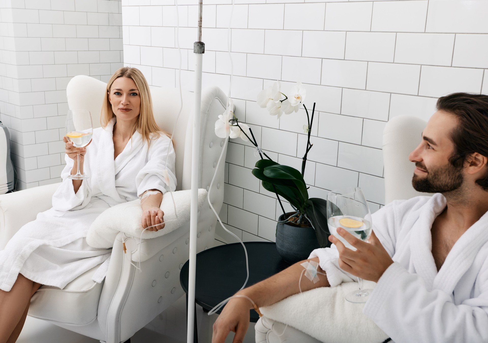 Couple during intravenous vitamin therapy. Beautiful woman with her boyfriend with glasses of refreshing drink with lemon in medical clinic for detox their organisms