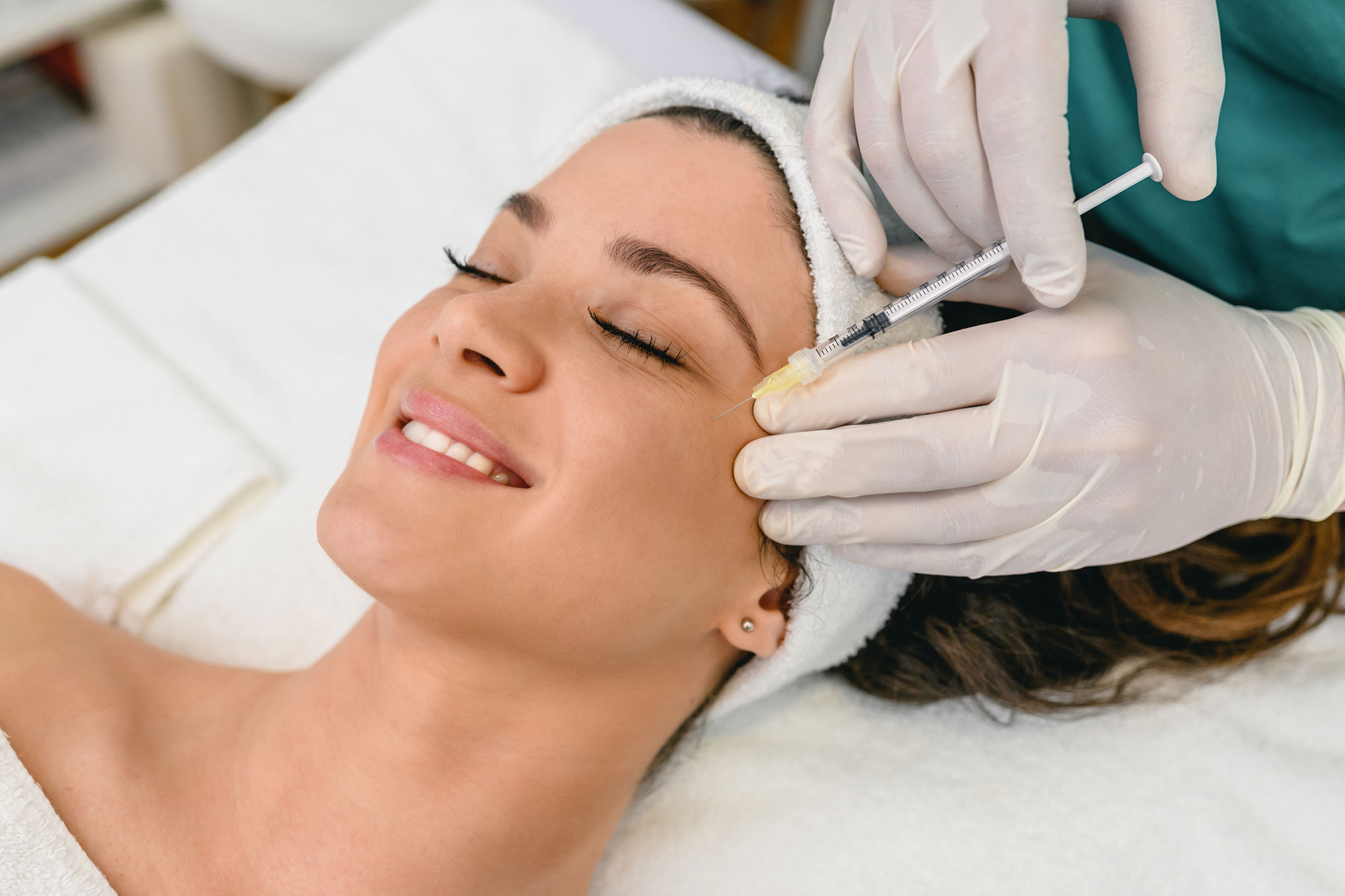 A woman receiving a facial injection treatment while smiling in a spa setting.