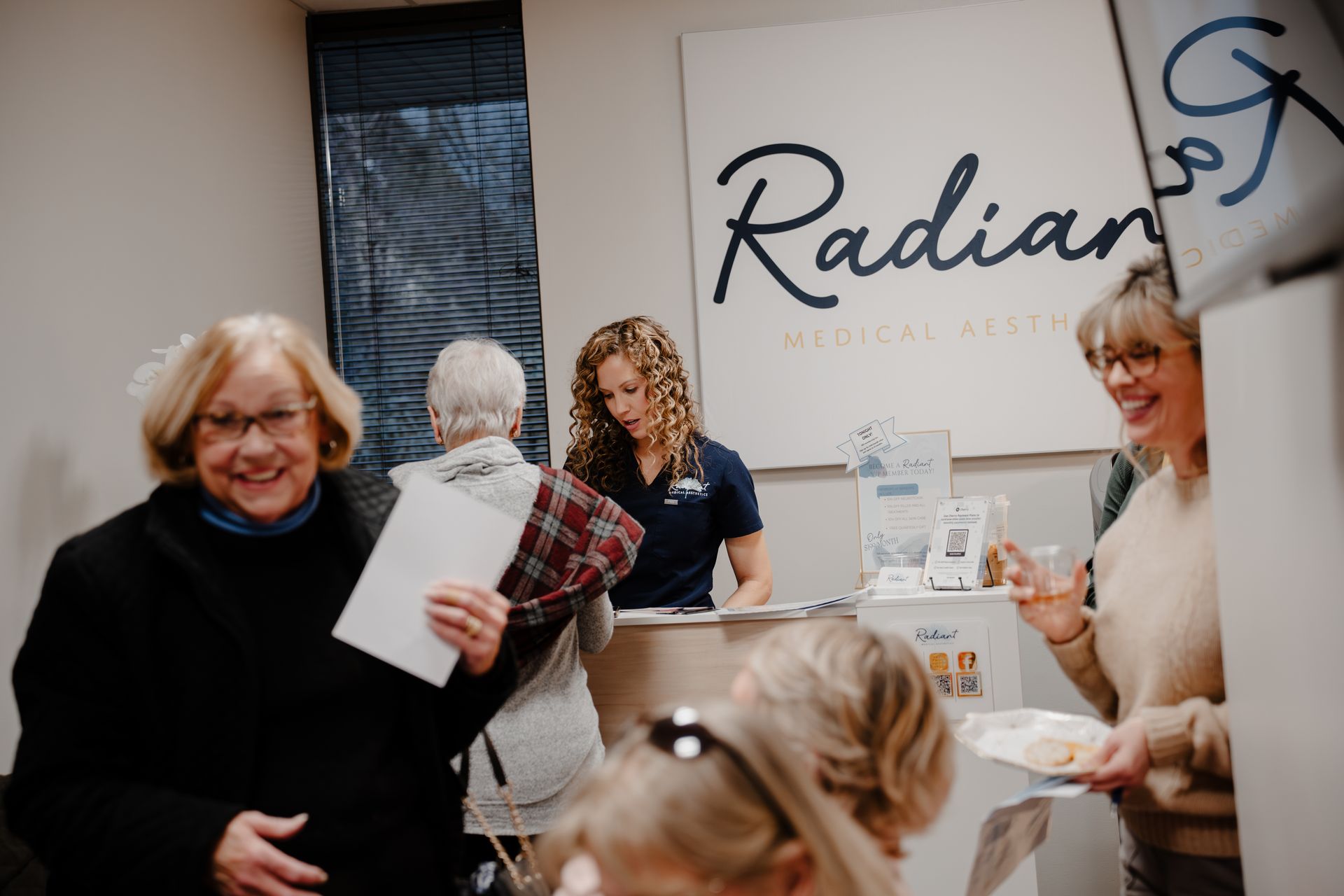 People at Radiant Medical Aesthetics reception desk, woman smiling with paper.