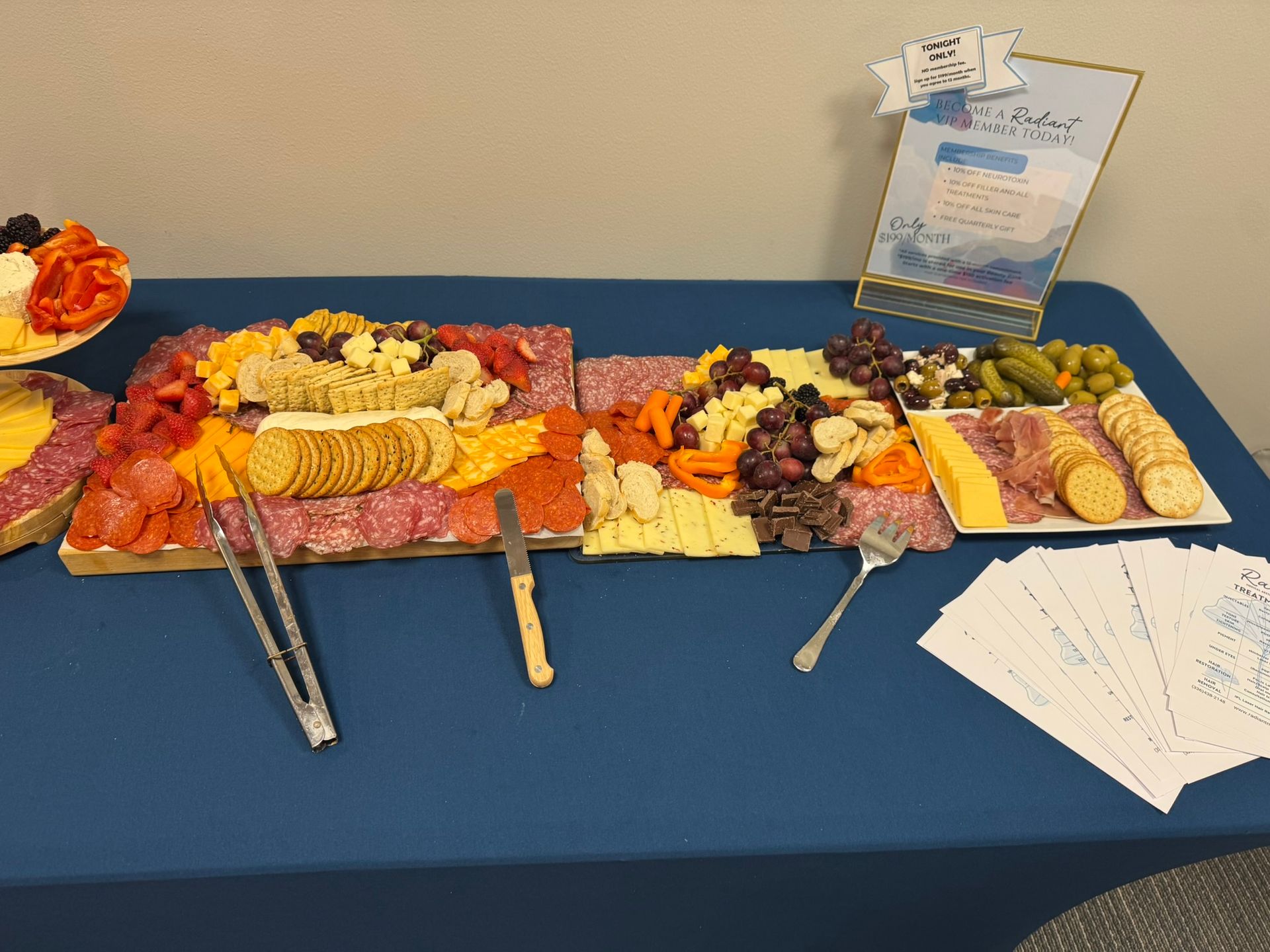 Charcuterie board with assorted cheeses, meats, fruits, and crackers on a blue tablecloth.