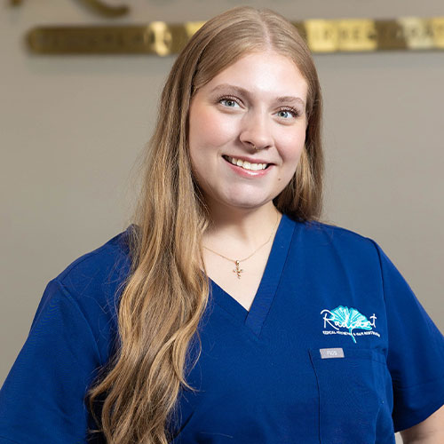 A smiling woman in a blue medical uniform with long hair.