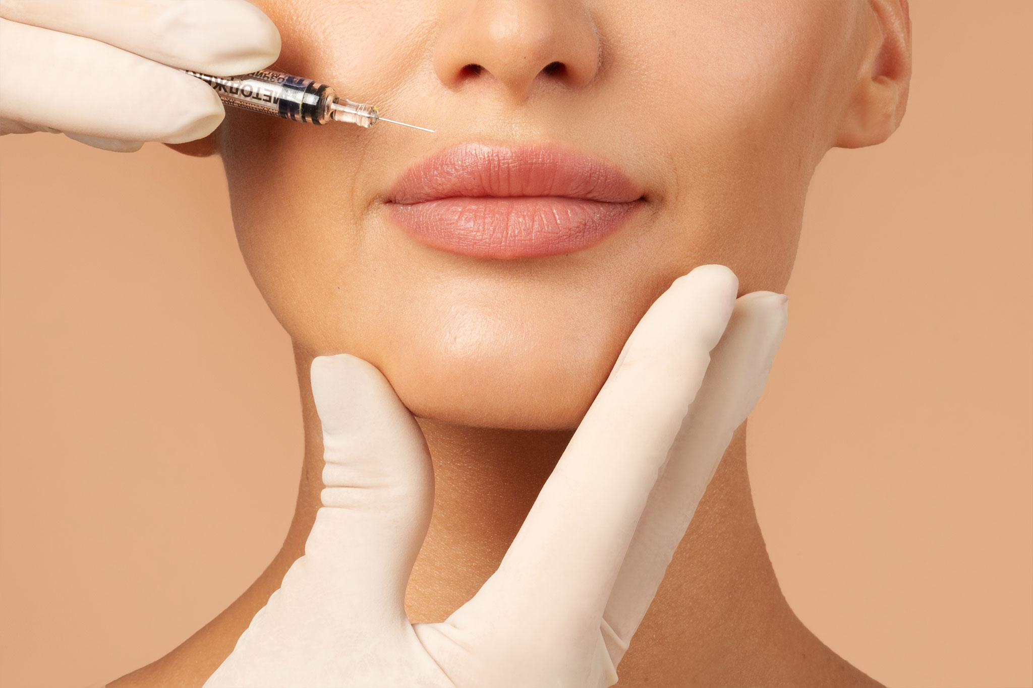 A person receiving dermal filler injection in lips by a gloved professional.