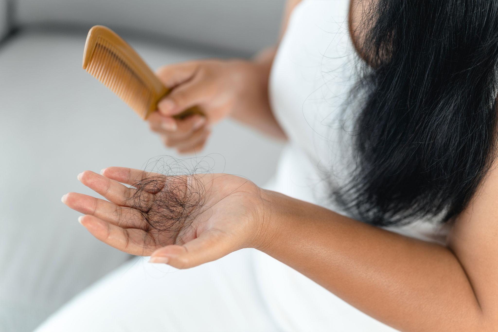 A woman holding a comb and hair in hand, indicating hair loss.