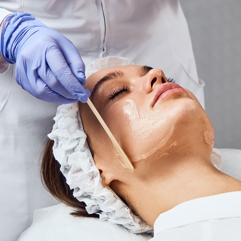 Person receiving a facial treatment with a mask applied by a professional in gloves.
