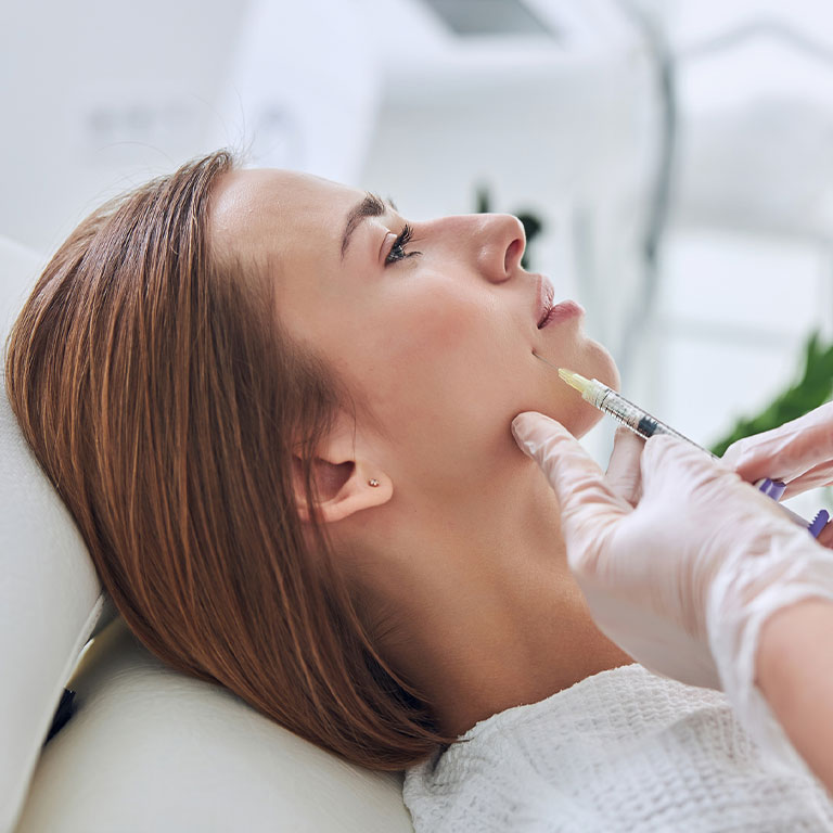 A woman receiving a cosmetic injection in the jaw at a clinic.