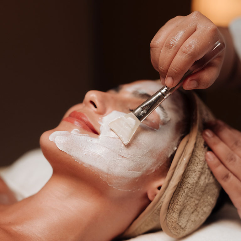 Person receiving facial treatment with a brush applying a white mask.