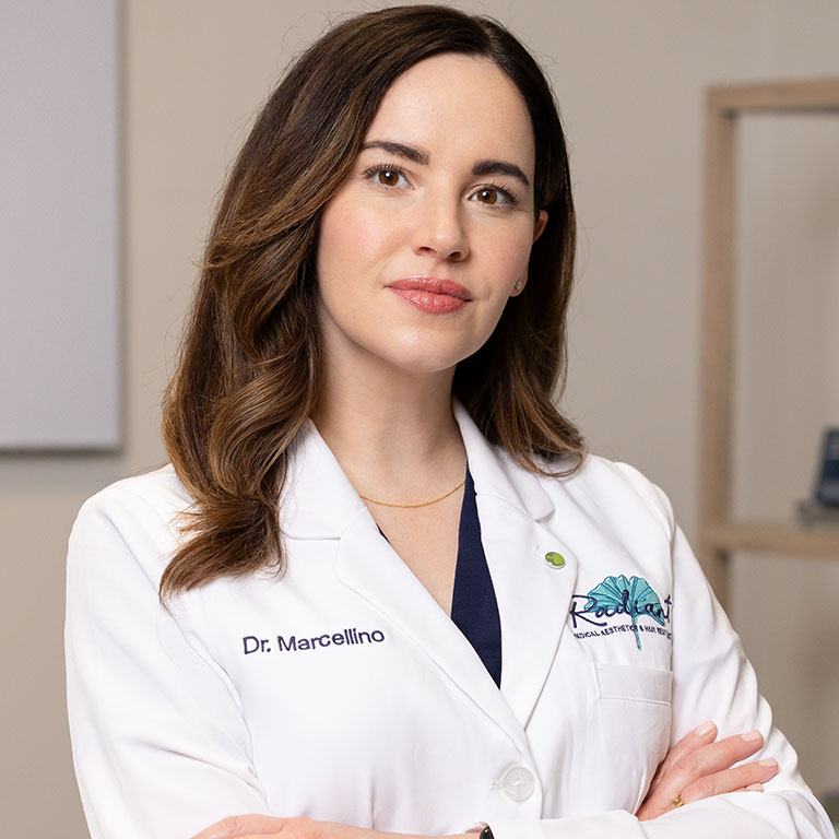 Dr. Marcellino wearing a white lab coat, standing confidently in an office setting.
