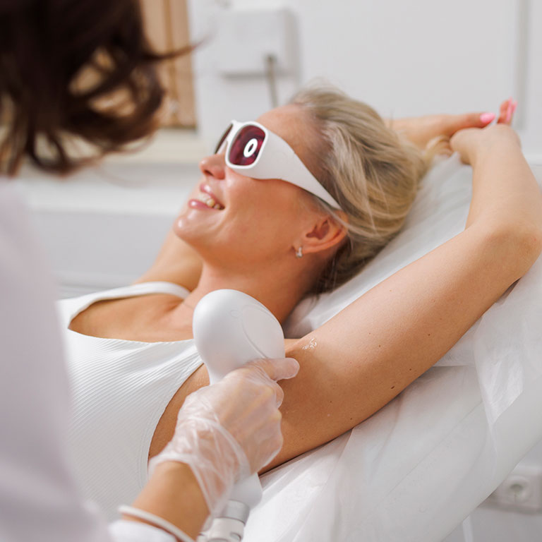 A woman receiving laser hair removal on her armpit in a clinic.