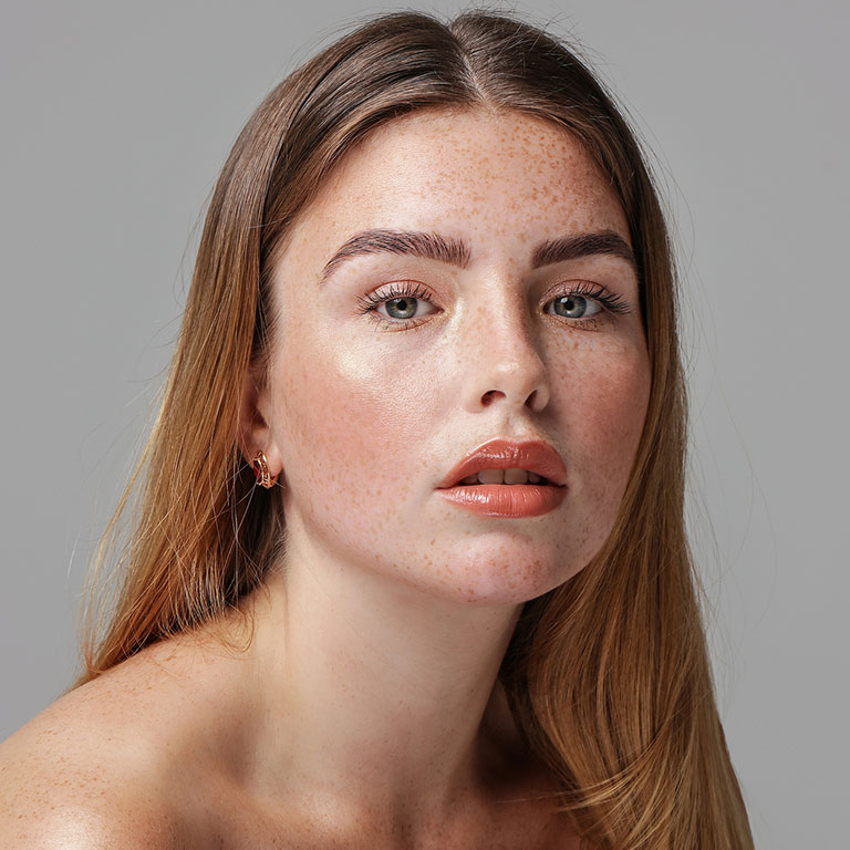 A woman with freckles and long hair posing against a gray background.