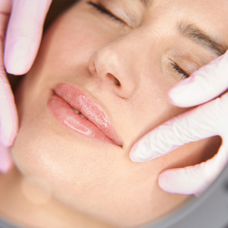 Facial skincare treatment on a woman with pink gloves.