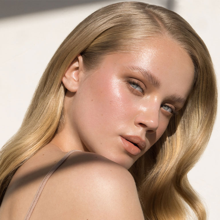 A woman with long blonde hair and glowing skin in a close-up portrait.