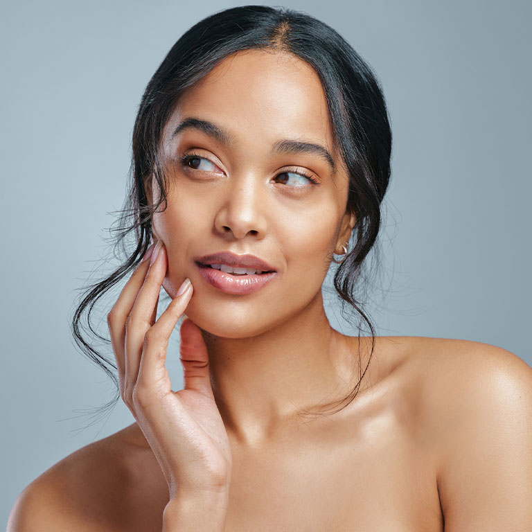 Woman with hand on face looking aside against gray background.