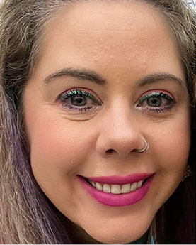A woman smiling with bright pink lipstick and a nose ring.