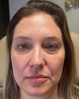 A woman with brown hair and neutral expression in a chair, indoors.