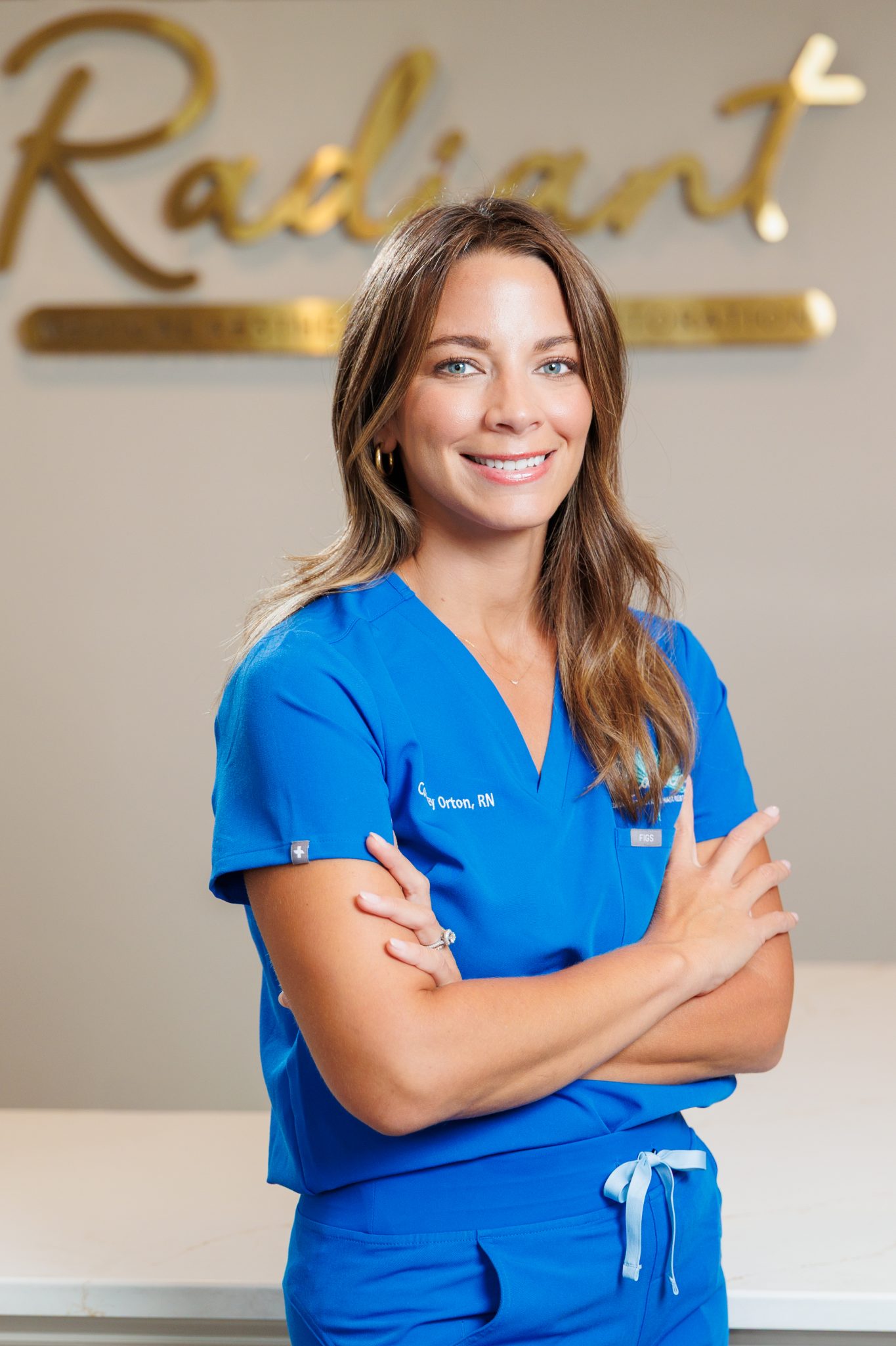 A woman in blue scrubs stands confidently, smiling in front of a sign.