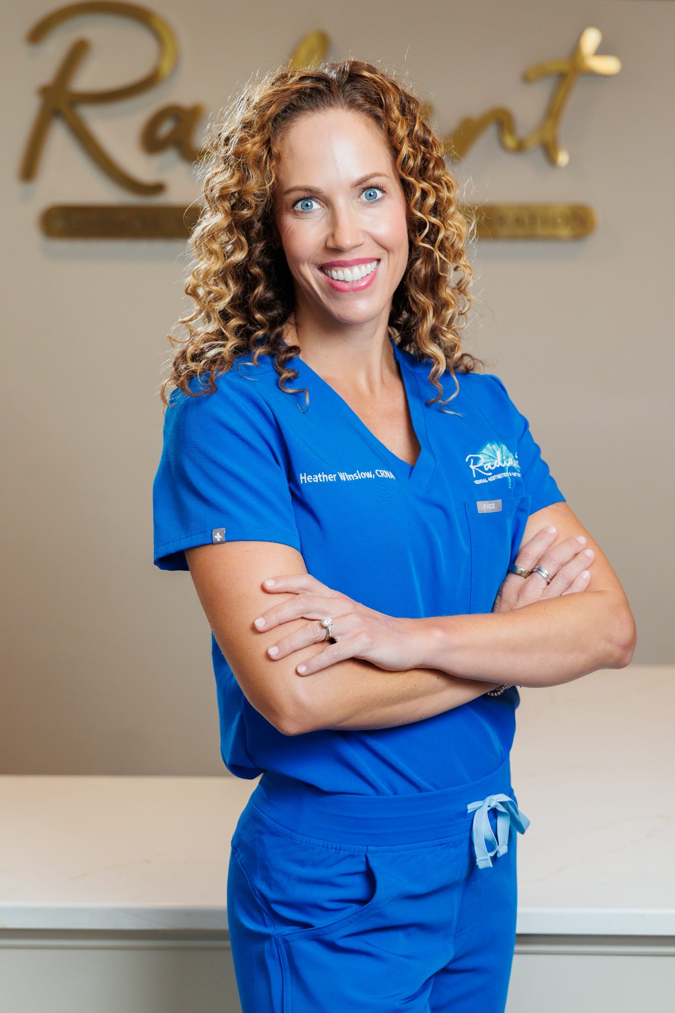 Heather Winslow smiling in blue medical scrubs with arms crossed.